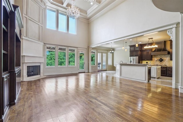 13209 Blue Canyon Cir, Oklahoma City, OK 73142 - unfurnished living room featuring a chandelier, a towering ceiling, crown molding, light wood-style floors, and a premium fireplace