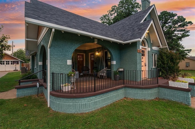 1828 S 7th St, Chickasha, OK 73018 - view of front of home with covered porch, a shingled roof, brick siding, a yard, and a chimney