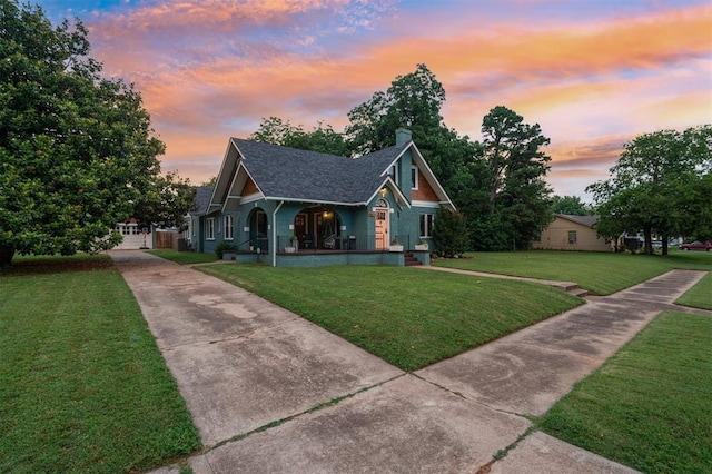 1828 S 7th St, Chickasha, OK 73018 - view of front of house with covered porch, a yard, driveway, roof with shingles, and a chimney