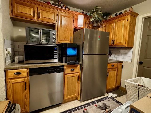 13501 E Memorial Rd, Jones, OK 73049 - kitchen featuring stainless steel appliances, backsplash, brown cabinets, and light tile patterned floors