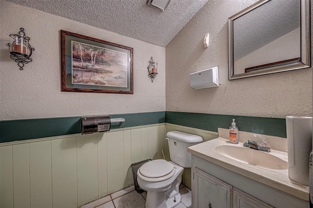 1028 N 11th St, Chickasha, OK 73018 - half bathroom featuring a textured ceiling, vanity, a wainscoted wall, tile patterned floors, and a textured wall