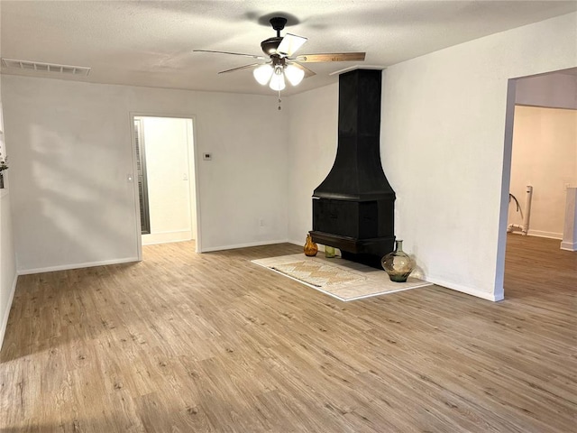 1402 S 14th St, Chickasha, OK 73018 - unfurnished living room featuring ceiling fan, a wood stove, and light wood-style floors