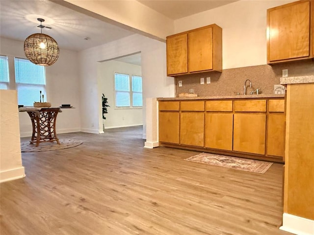 1402 S 14th St, Chickasha, OK 73018 - kitchen featuring light wood-type flooring, tasteful backsplash, light countertops, brown cabinets, and decorative light fixtures