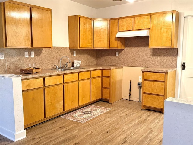 1402 S 14th St, Chickasha, OK 73018 - kitchen featuring under cabinet range hood, light wood-style floors, tasteful backsplash, light countertops, and brown cabinets