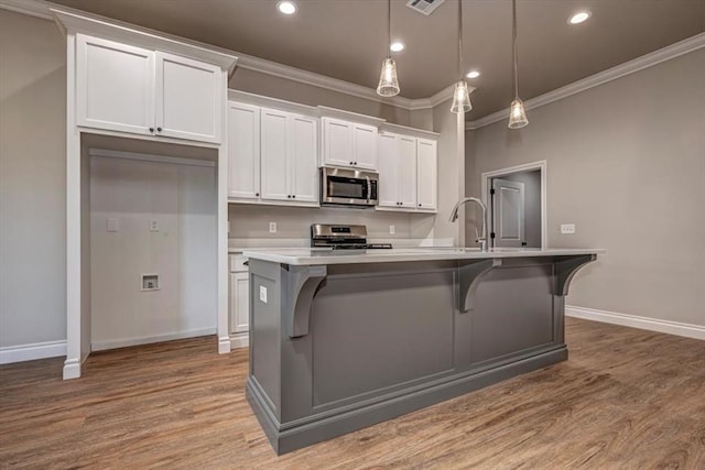 2001 W Crossbow Way, Mustang, OK 73065 - kitchen with appliances with stainless steel finishes, crown molding, wood finished floors, white cabinetry, and a center island with sink