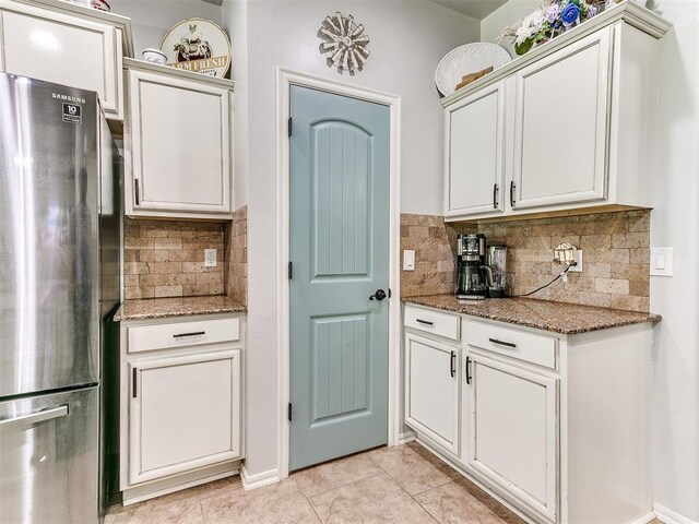 21945 N Fork Rd, Luther, OK 73054 - kitchen with freestanding refrigerator, backsplash, light tile patterned floors, stone counters, and white cabinetry
