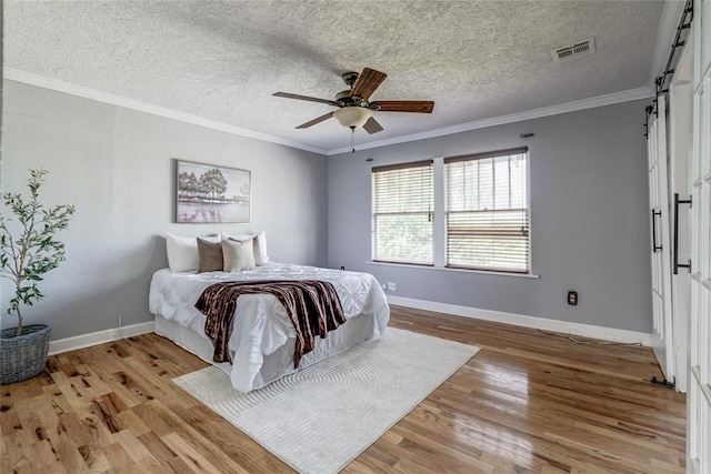 904 NW 19th St, Oklahoma City, OK 73106 - bedroom featuring a barn door, light wood-style floors, crown molding, a textured ceiling, and ceiling fan