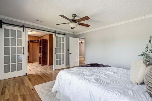 904 NW 19th St, Oklahoma City, OK 73106 - bedroom with a barn door, crown molding, wood finished floors, a textured ceiling, and a ceiling fan