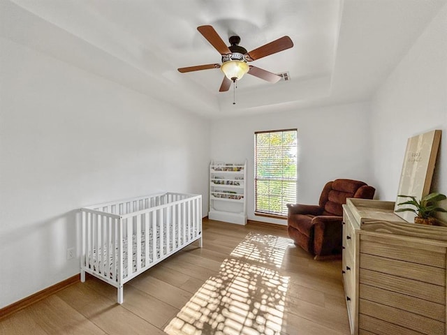 12200 Whispering Pnes, Guthrie, OK 73044 - bedroom featuring a tray ceiling, light wood-style floors, a nursery area, and a ceiling fan