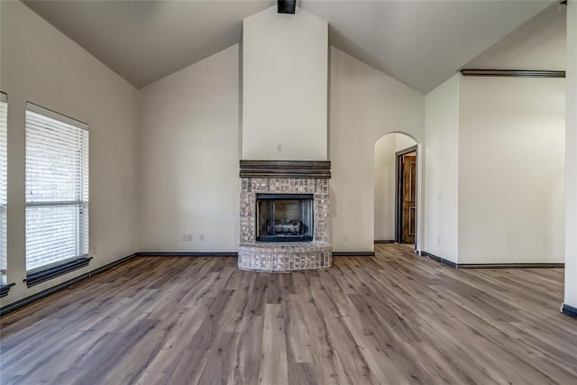 3904 Normandy Rd, Edmond, OK 73013 - unfurnished living room featuring arched walkways, wood finished floors, a fireplace, and high vaulted ceiling