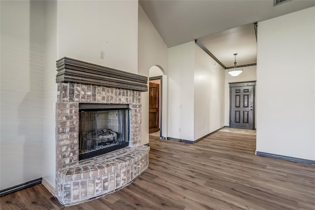 3904 Normandy Rd, Edmond, OK 73013 - unfurnished living room with wood finished floors, a brick fireplace, arched walkways, and a high ceiling