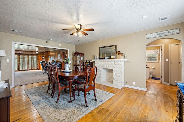 3409 S 4th St, Chickasha, OK 73018 - dining space with a ceiling fan, arched walkways, hardwood / wood-style flooring, a textured ceiling, and a stone fireplace