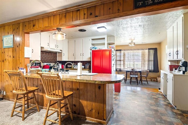 3409 S 4th St, Chickasha, OK 73018 - kitchen featuring white cabinets, wood walls, under cabinet range hood, tasteful backsplash, and a breakfast bar area