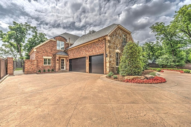 6516 NW Grand Blvd, Nichols Hills, OK 73116 - view of home's exterior with a gate, driveway, a garage, brick siding, and stone siding
