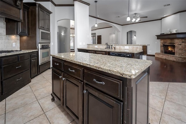 16312 Old Elm Ln, Edmond, OK 73013 - kitchen featuring appliances with stainless steel finishes, ceiling fan, light tile patterned floors, arched walkways, and ornamental molding