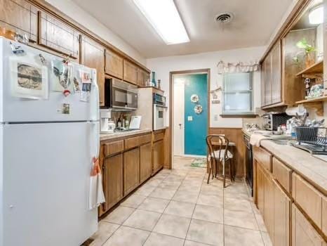 1329 SW 77th Ter, Oklahoma City, OK 73159 - kitchen featuring appliances with stainless steel finishes, light countertops, light tile patterned floors, open shelves, and brown cabinets