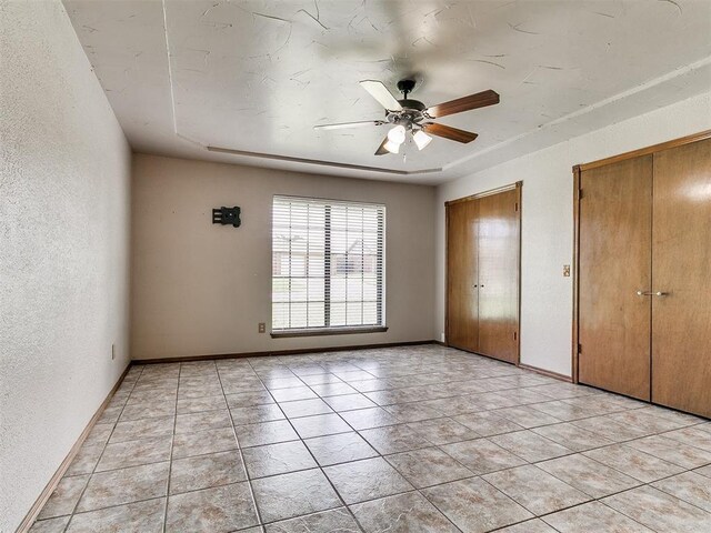 2228 Butternut Pl, Edmond, OK 73013 - unfurnished bedroom with two closets, a textured wall, light tile patterned flooring, and a ceiling fan