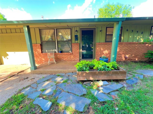 6338 Norman Rd, Warr Acres, OK 73122 - view of exterior entry featuring board and batten siding, brick siding, covered porch, and an attached garage