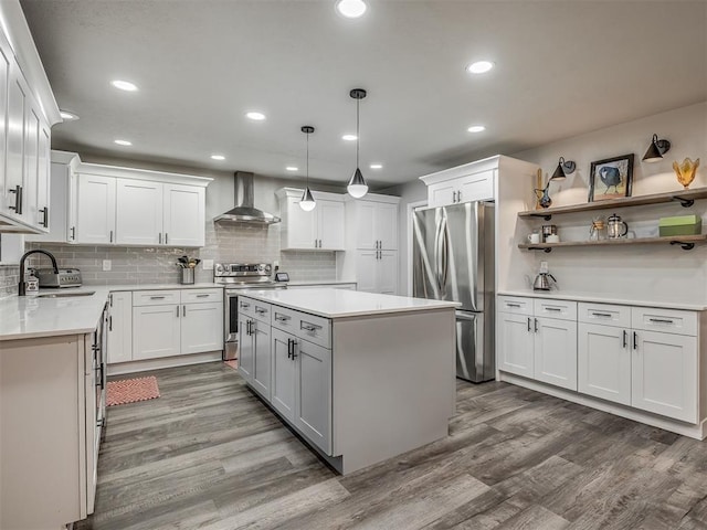 10505 Lyndon Rd, The Village, OK 73120 - kitchen featuring appliances with stainless steel finishes, wall chimney exhaust hood, wood finished floors, a kitchen island, and light countertops