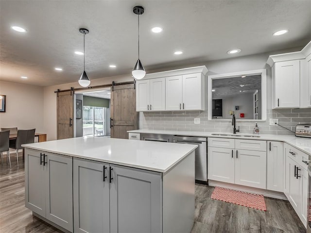 10505 Lyndon Rd, The Village, OK 73120 - kitchen featuring stainless steel dishwasher, a kitchen island, a barn door, wood finished floors, and light countertops