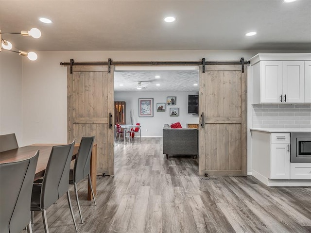 10505 Lyndon Rd, The Village, OK 73120 - kitchen with a barn door, light wood-type flooring, white cabinetry, backsplash, and recessed lighting