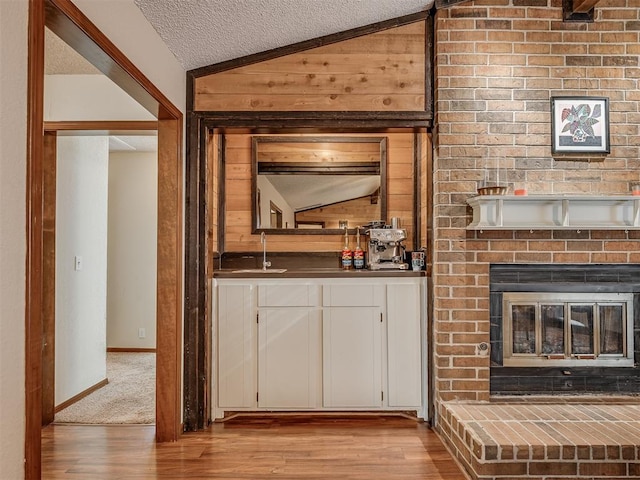 2104 Tanglewood Dr, Edmond, OK 73013 - unfurnished living room featuring vaulted ceiling, wood finished floors, a textured ceiling, wooden walls, and a brick fireplace
