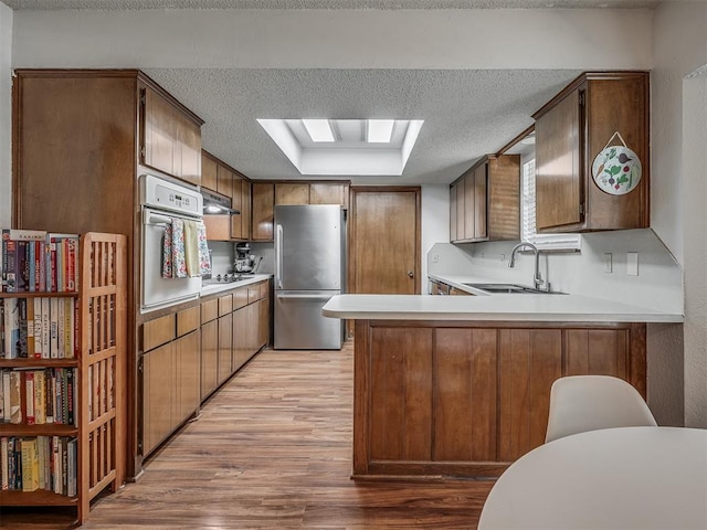 2104 Tanglewood Dr, Edmond, OK 73013 - kitchen featuring freestanding refrigerator, oven, light wood-style floors, under cabinet range hood, and a textured ceiling