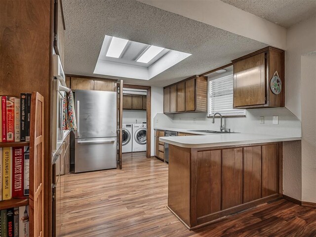 2104 Tanglewood Dr, Edmond, OK 73013 - kitchen with stainless steel appliances, independent washer and dryer, a textured ceiling, a peninsula, and light wood-style flooring