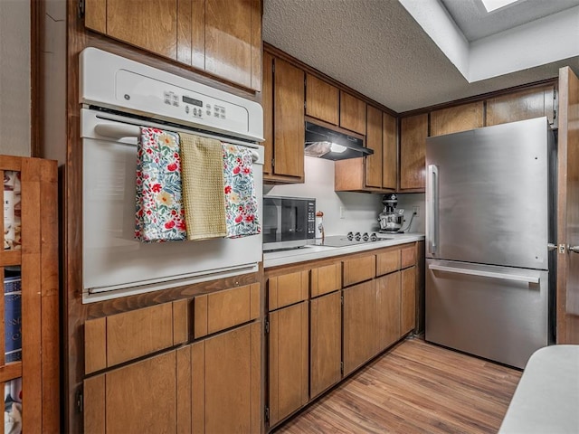 2104 Tanglewood Dr, Edmond, OK 73013 - kitchen with stainless steel appliances, under cabinet range hood, light countertops, light wood-type flooring, and brown cabinetry