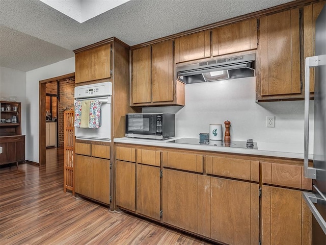 2104 Tanglewood Dr, Edmond, OK 73013 - kitchen featuring stainless steel microwave, oven, under cabinet range hood, light wood-type flooring, and a textured ceiling