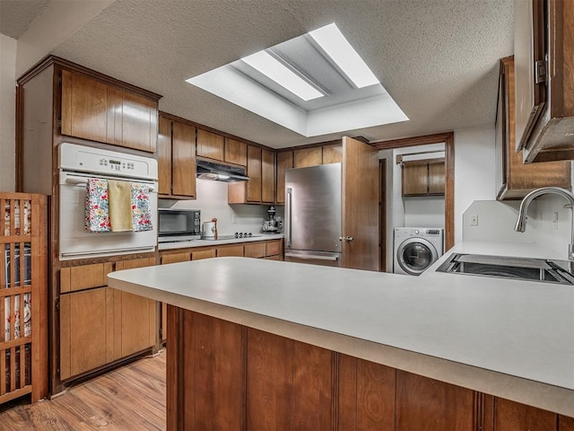 2104 Tanglewood Dr, Edmond, OK 73013 - kitchen featuring appliances with stainless steel finishes, washer / clothes dryer, a peninsula, a textured ceiling, and light wood-type flooring