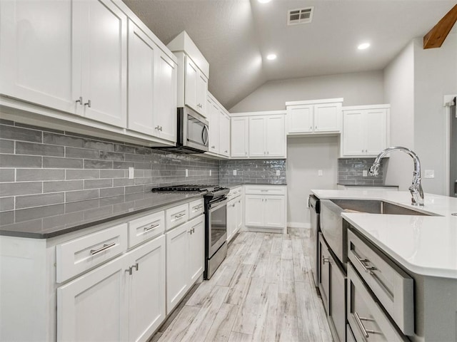 6713 NW 149th St, Oklahoma City, OK 73142 - kitchen featuring appliances with stainless steel finishes, tasteful backsplash, white cabinetry, light wood-style flooring, and vaulted ceiling