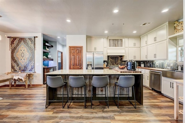 1187 County St Unit 2976, Blanchard, OK 73010 - kitchen with appliances with stainless steel finishes, a kitchen island, a breakfast bar area, decorative backsplash, and white cabinets
