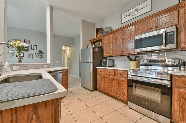 4616 Midway Dr, Norman, OK 73072 - kitchen featuring appliances with stainless steel finishes, light countertops, decorative backsplash, light tile patterned flooring, and brown cabinetry