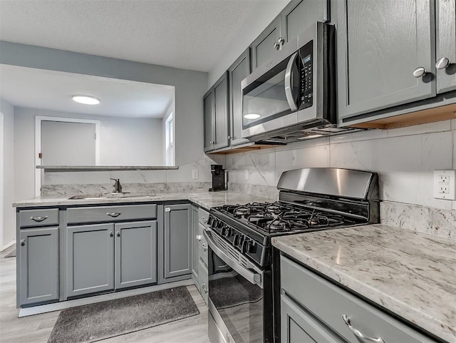 1508 Loftin Dr, Midwest City, OK 73130 - kitchen featuring range with gas stovetop, stainless steel microwave, gray cabinets, light stone counters, and light wood finished floors