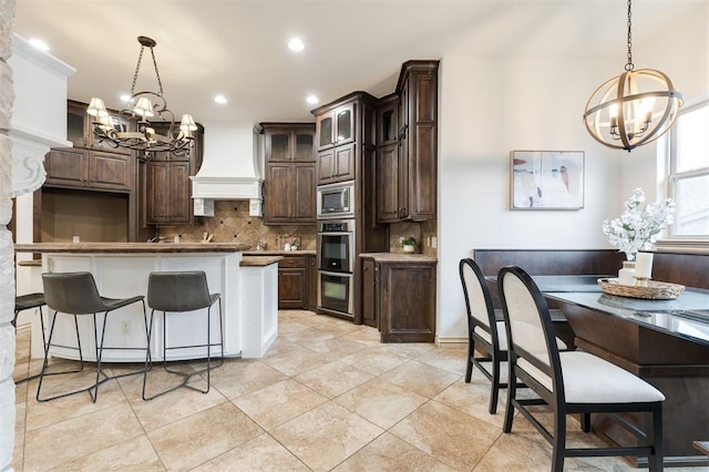 3101 White Cedar Dr, Moore, OK 73160 - kitchen with a chandelier, custom exhaust hood, tasteful backsplash, dark brown cabinets, and recessed lighting