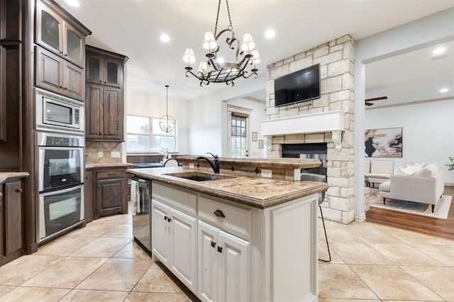 3101 White Cedar Dr, Moore, OK 73160 - kitchen with appliances with stainless steel finishes, a chandelier, open floor plan, a fireplace, and dark brown cabinetry