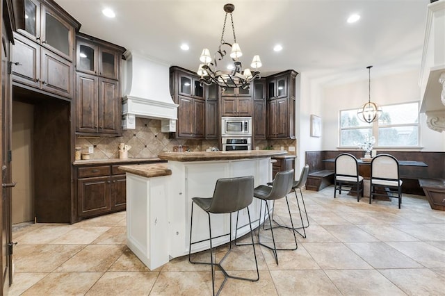 3101 White Cedar Dr, Moore, OK 73160 - kitchen with appliances with stainless steel finishes, a chandelier, custom exhaust hood, dark brown cabinetry, and tasteful backsplash