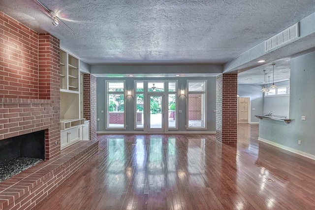 823 S Flood Ave, Norman, OK 73069 - unfurnished living room with a textured ceiling, wood-type flooring, a brick fireplace, and built in features