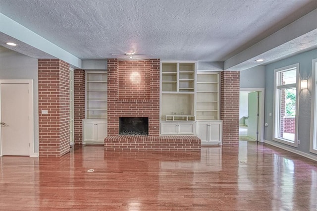 823 S Flood Ave, Norman, OK 73069 - unfurnished living room with wood finished floors, a textured ceiling, a brick fireplace, built in shelves, and recessed lighting