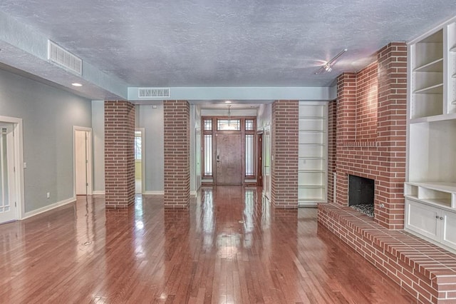 823 S Flood Ave, Norman, OK 73069 - unfurnished living room featuring a textured ceiling, a brick fireplace, hardwood / wood-style floors, and built in shelves