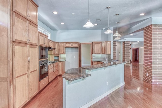 823 S Flood Ave, Norman, OK 73069 - kitchen with black appliances, light wood-type flooring, a breakfast bar area, dark stone counters, and pendant lighting