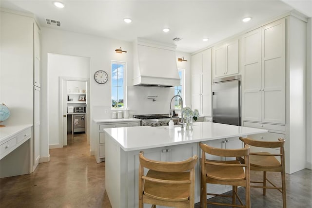 1006 Dorsi Way, Newcastle, OK 73065 - kitchen featuring built in refrigerator, custom exhaust hood, finished concrete flooring, a center island with sink, and light countertops