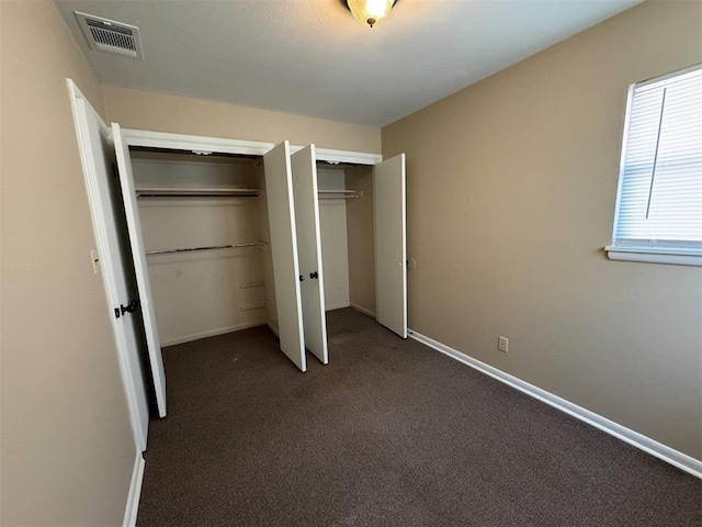 unfurnished bedroom with dark colored carpet and multiple closets