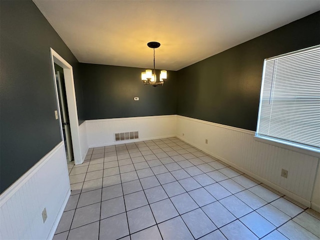 unfurnished room with a wainscoted wall, a chandelier, and light tile patterned floors