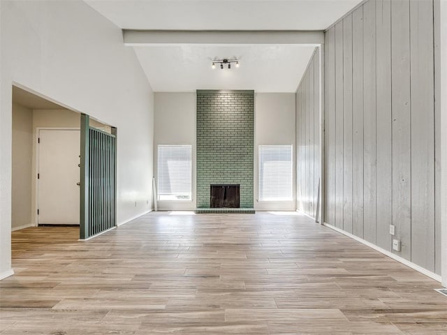 11516 N Barnes Ave, Oklahoma City, OK 73120 - unfurnished living room with high vaulted ceiling, wood walls, wood finished floors, beam ceiling, and a brick fireplace