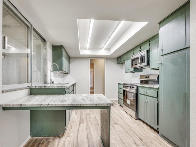 11516 N Barnes Ave, Oklahoma City, OK 73120 - kitchen with green cabinetry, appliances with stainless steel finishes, light wood-style flooring, a tray ceiling, and light stone counters