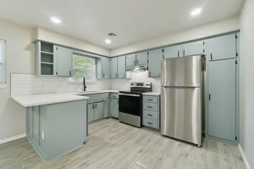 107 Cimarron Ter, Cashion, OK 73016 - kitchen with stainless steel appliances, under cabinet range hood, a peninsula, light countertops, and light wood finished floors