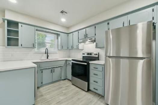 107 Cimarron Ter, Cashion, OK 73016 - kitchen with stainless steel appliances, under cabinet range hood, decorative backsplash, light wood-style flooring, and light countertops
