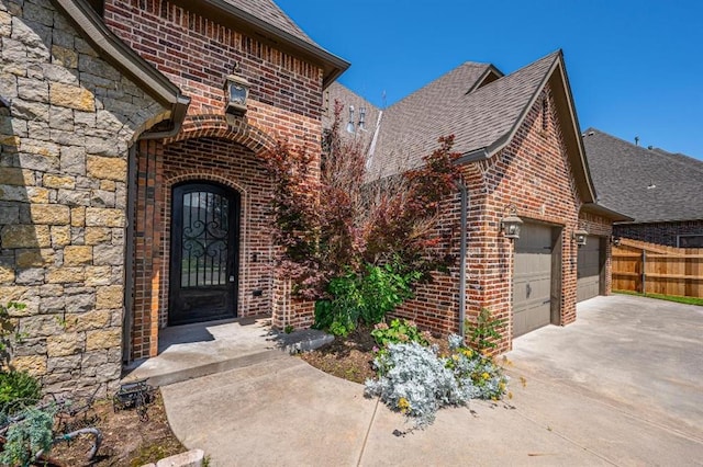 3205 Sycamore Dr, Moore, OK 73160 - view of exterior entry with concrete driveway, brick siding, a garage, roof with shingles, and stone siding